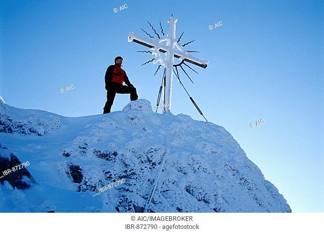 Man standing next to the summit cross on Mt. Steinerner Jaeger, pre-Alps near Reichraming in the winter, Upper Austria, Austria, Europe