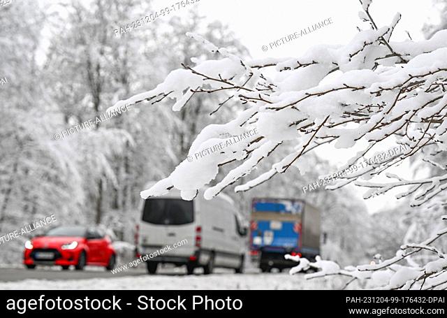 04 December 2023, Baden-Württemberg, Bebenhausen: Cars drive through a snow-covered forest on a road near Bebenhausen. Photo: Bernd Weißbrod/dpa