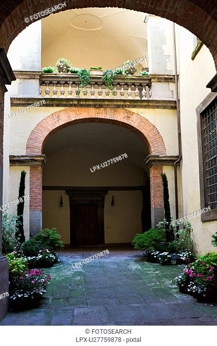 Detail of inner courtyard of Italian Renaissance palazzo, decorated with flowers, with arched windows and balustrade, brick and stucco, Todi, Umbria