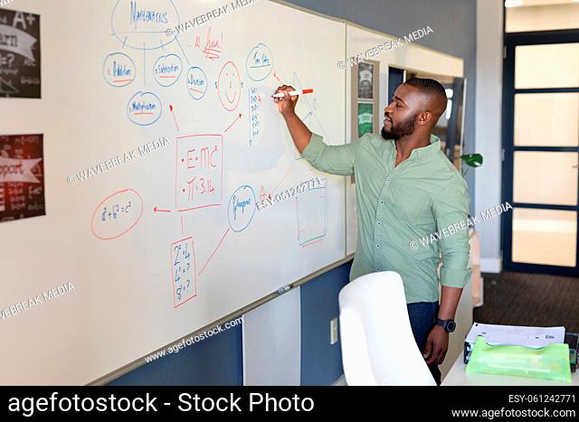 African american young male teacher writing on whiteboard while teaching in classroom