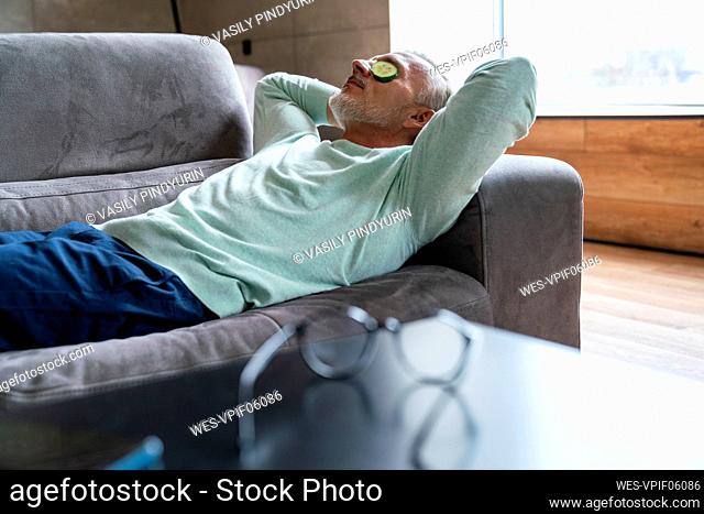 Man with cucumber slices on eyes lying on sofa at home