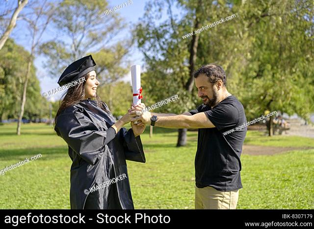 Young girl recently graduated, dressed in cap and gown, with her degree in her hands, celebrating with her family on the university campus