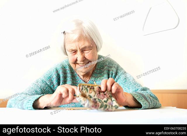 Cheerful elderly 96 years old woman sitting at table at home happy with her pension savings in her wallet after paying bills