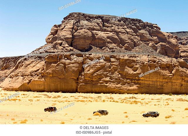 Three Vehicles driving past Wadi Teshuinat, Akakus, Sahara desert, Fezzan, Libya