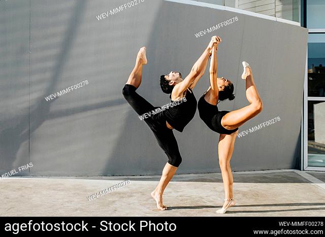 Professional gymnasts standing on one leg while balancing by gray wall