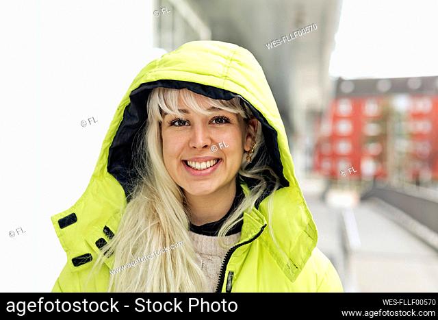 Close-up of smiling young woman wearing yellow winter coat in city