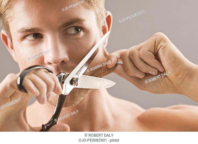 Portrait of man holding scissors and pulling skin on face