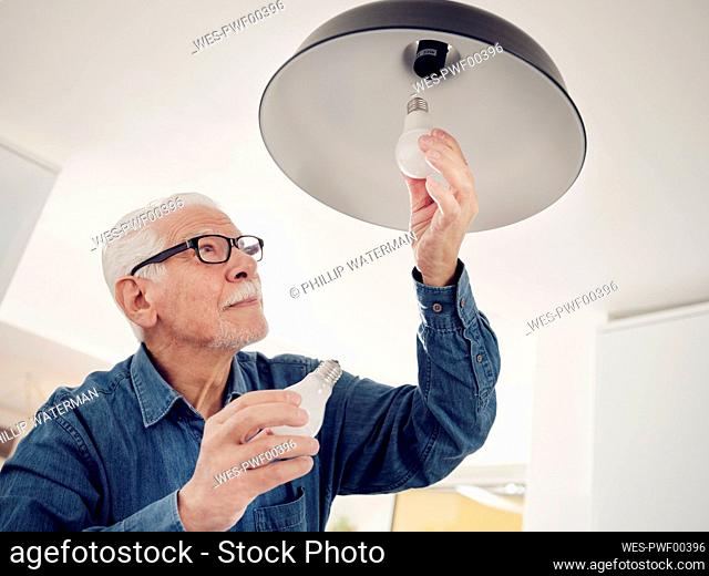 Senior man changing old lightbulb for a LED energy saving lightbulb