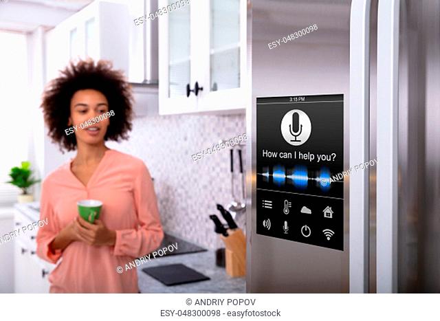 Young Woman Holding Green Coffee In Hand Looking At Refrigerator With Voice Recognition Function