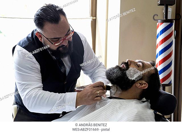 Barber putting shaving foam in man's beard