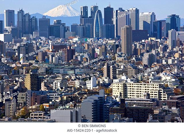 A telephoto view on a clear winter day captures a snow-capped Mt. Fuji rising dramatically beyond the skyscrapers (including Tokyo City Hall) of the Shinjuku...