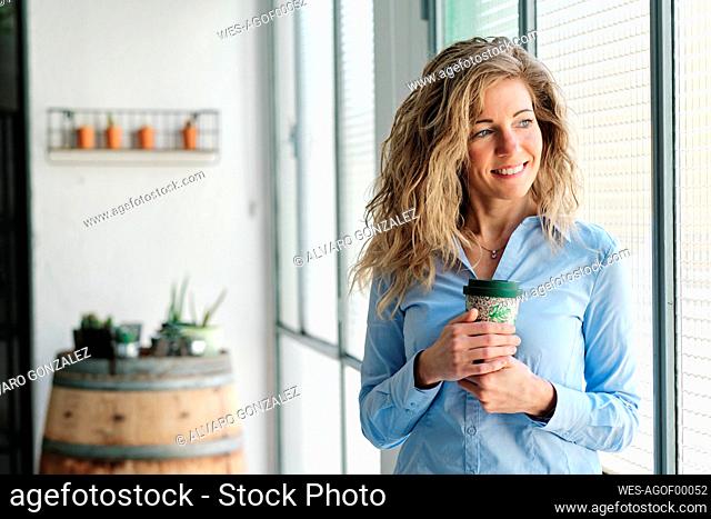 Smiling blond woman with reusable cup looking through window