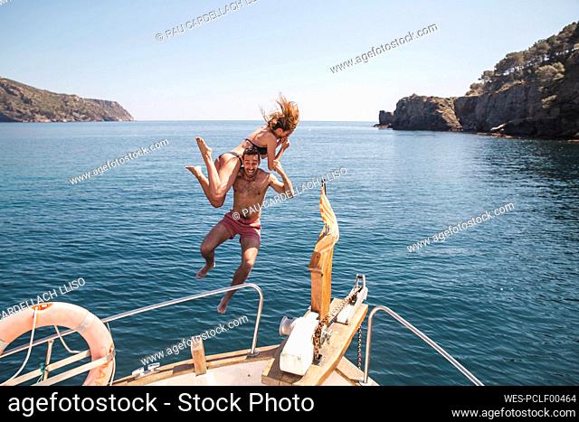 Man and woman jumping in sea from boat at vacation
