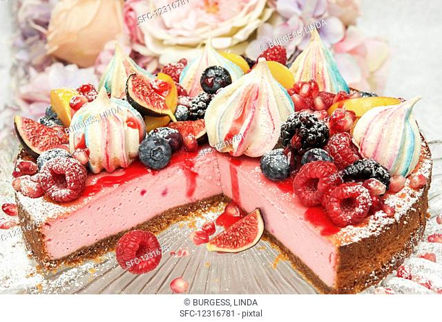 Strawberry cheesecake with merangue kisses and fresh fruit on the top on a glass cake stand in front of flowers