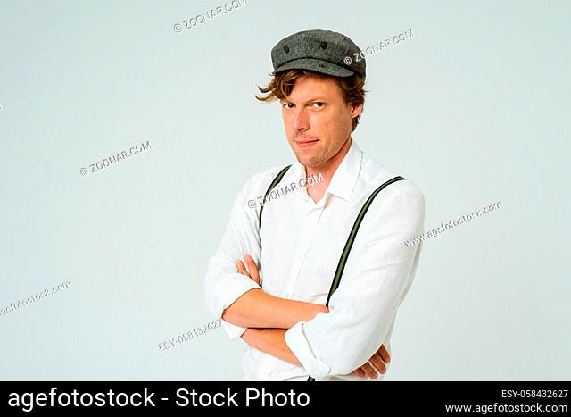 Hipster man posing with hands folded dressed in white shirt and grey wool cap isolated on white background. Copy space at left side