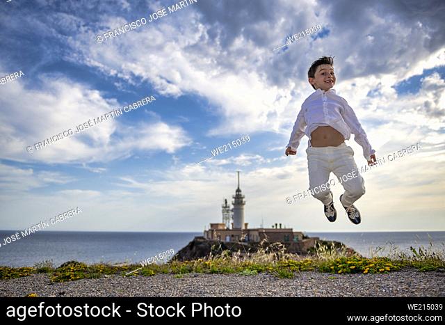 Child jumps for photo one day with clouds with lighthouse and sea in background
