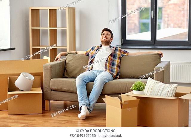 happy man with boxes sitting on sofa at new home