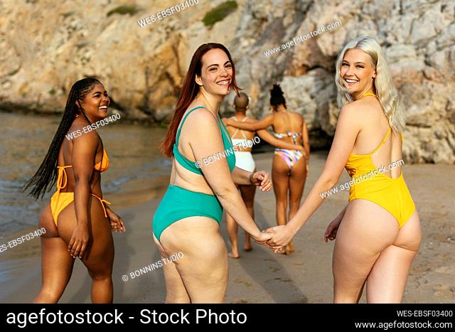 Happy friends holding hands at beach