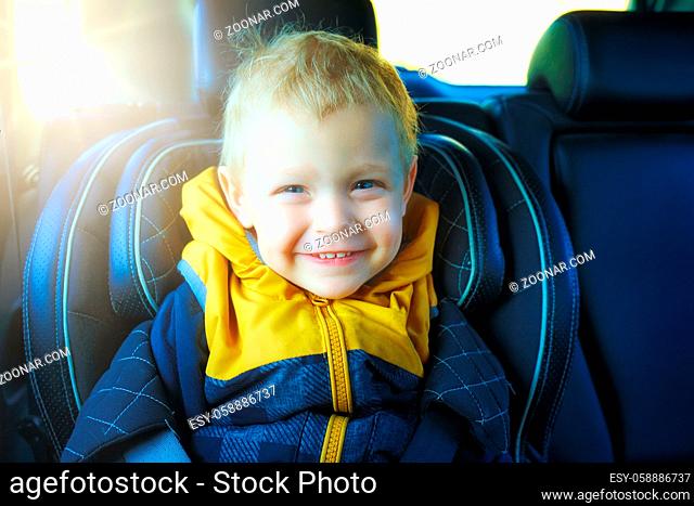 A blond toddler sits in a child's car seat and smiles. This is the happy boy in the car. Care and safety while driving. Children's portrait