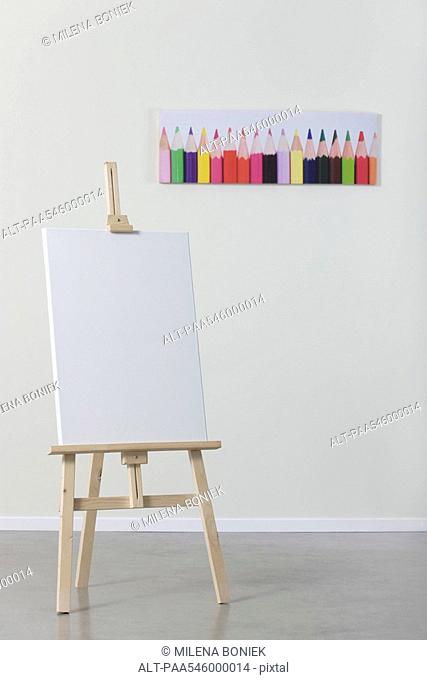 Blank canvas on easel, poster of colored pencils in background