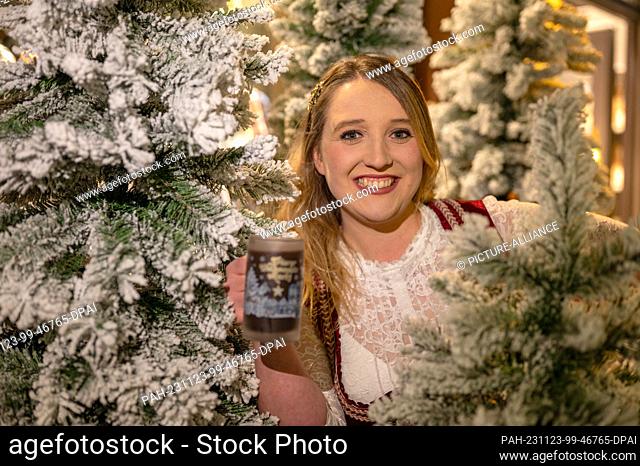 21 November 2023, Rhineland-Palatinate, Trier: The new German mulled wine queen Louisa Kress holds a mulled wine in the middle of artificial Christmas trees