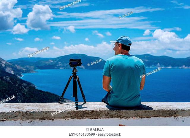 Summer holiday visiting Greece. Male freelance photographer enjoying capturing time lapse moving cloudscape coastline and Mediterranean sea with camera on...