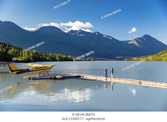 A woman and a man stand on a dock where a float plane is docked, Trail Lake Float Plane Base, Moose Pass, Kenai Peninsula, Southcentral Alaska, USA
