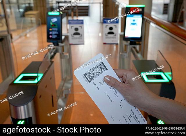 28 April 2022, Hamburg: A woman holds up a boarding pass in front of the biometric face field recognition system at the security checkpoint in the departure...