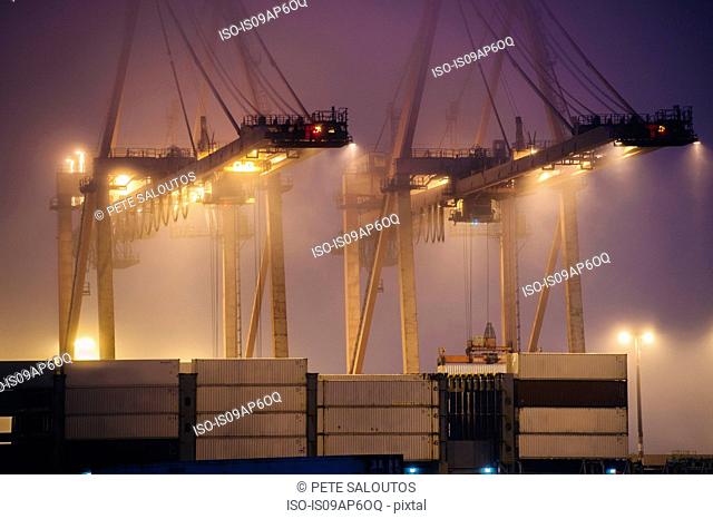 Misty view of harbor cranes and stacked cargo containers at night, Seattle, Washington, USA