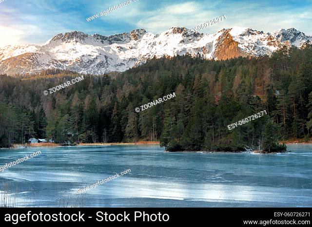 Winter landscape with a frozen lake surrounded by green fir forest and the snowy peaks of the Alps mountains, near Biberwier village, Austria