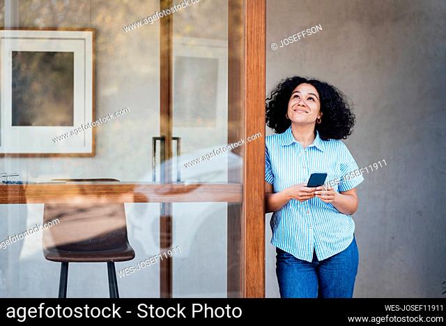 Smiling woman with smart phone standing at doorway
