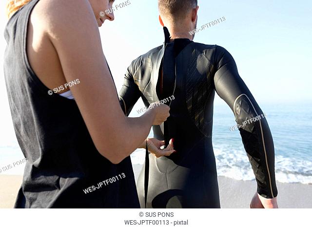 Woman zipping up man's wetsuit at the beach