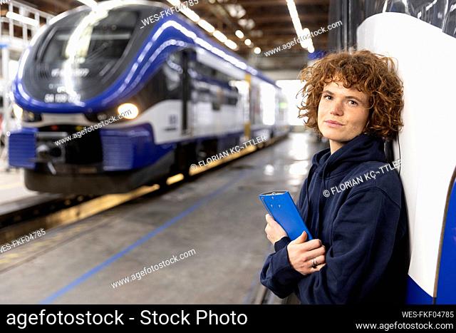 Engineer holding file folder leaning on monorail at industry