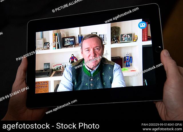 29 March 2020, Bavaria, Munich: A woman is watching the speech of Kevin Spacey, actor, on a tablet at the virtual founder's meeting of Bits & Pretzels