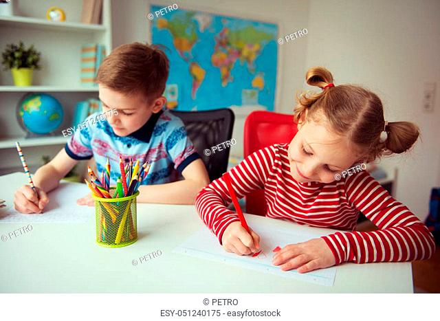 Two cute children drawing with colorful pencils at home