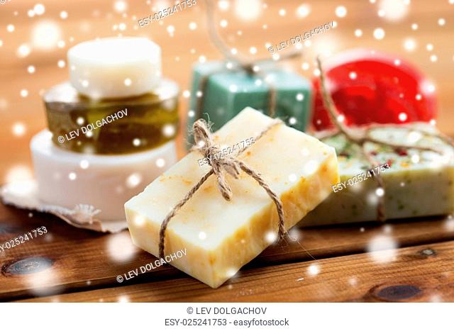 beauty, spa, bodycare, bath and natural cosmetics concept - close up of handmade soap bars on wooden table over snow
