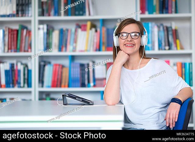 female student study in library using tablet and searching internet while Listening music and lessons on white headphones