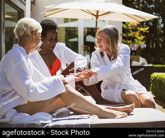 Senior women friends in spa bathrobes on sunny hotel patio