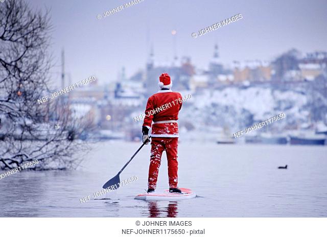 Man dressed as Santa Claus paddling on lake
