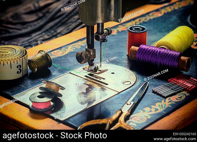 Closeup of an old sewing machine and accessories for sewing, scissors, needles and a tailor tape on a table. The concept of sewing accessories