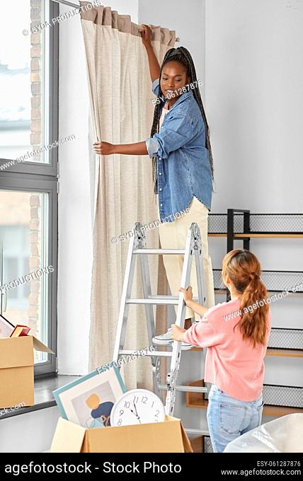 woman on ladder hanging curtains at home