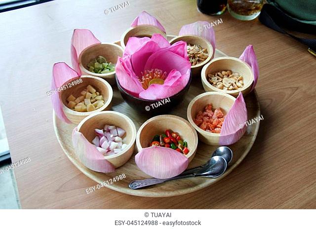 Miang kham traditional snack from Thailand or food wrapped in purple lotus leaves bite-size savoury appetizer in wooden dish and bowl on table of restaurant in...