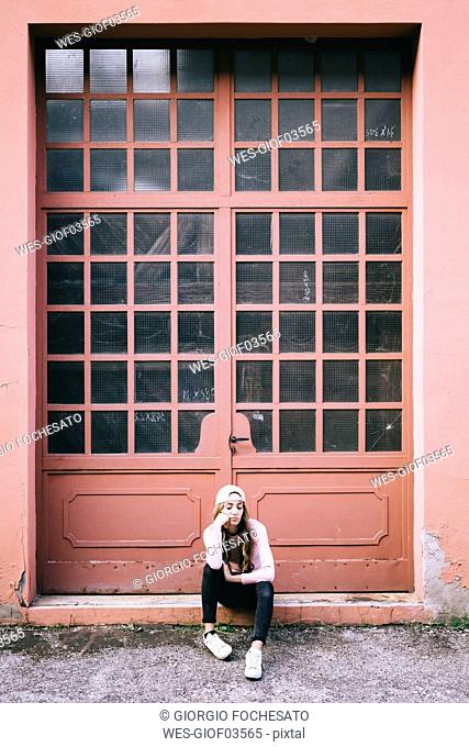 Fashionable young woman sitting in front of entrance gate