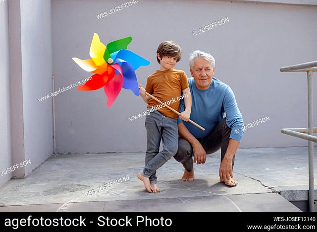 Smiling boy with multi colored pinwheel toy by grandfather at corridor