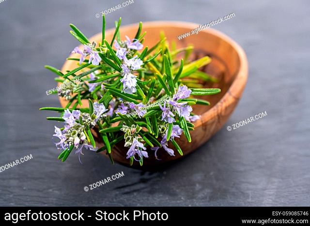Fresh purple blooming rosemary twigs in an olive wood bowl on a black slate background