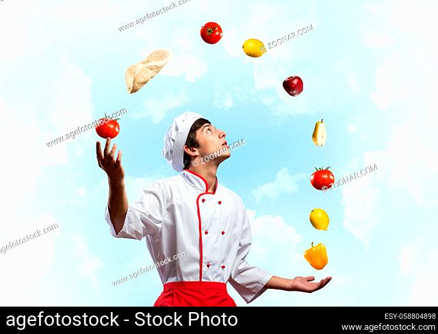 Young male chef juggles with food ingredients. Handsome chef in white hat and red apron on blue sky background. Professional cooking classes advertising