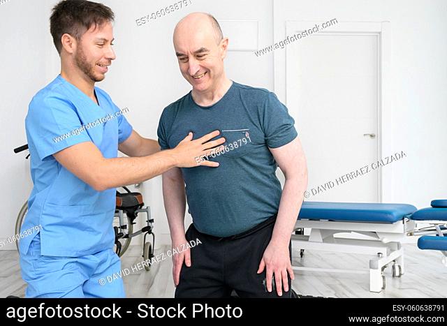 Physical therapist helping to disabled male patient, supporting during exercise therapy. High quality photo