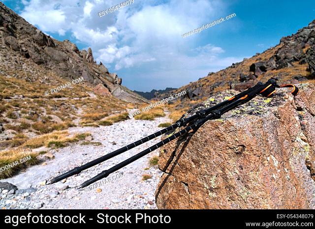 Professional sticks for climbing a mountain near a stone on a high mountain path against a blue sky and white clouds. The concept of active recreation and...