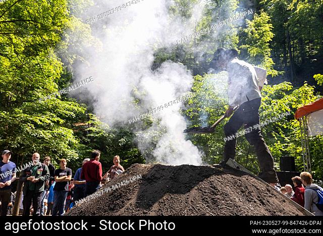 27 May 2023, Saxony, Tharandt: 16-year-old Niklas Papperitz stands on the charcoal pile in the Breiten Grund in the Tharandt Forest and throws hot pieces of...