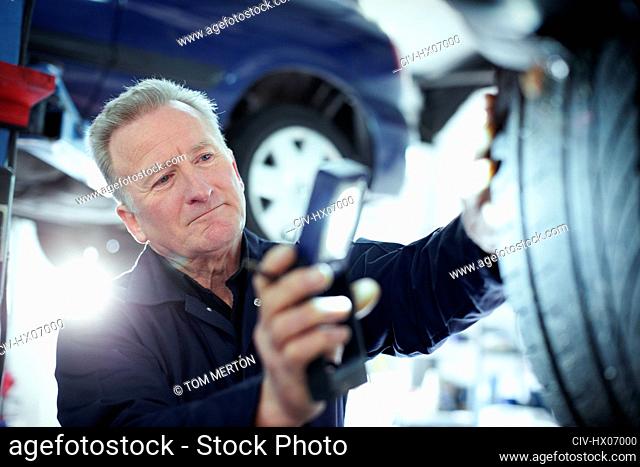 Male mechanic with flashlight examining tire in auto repair shop